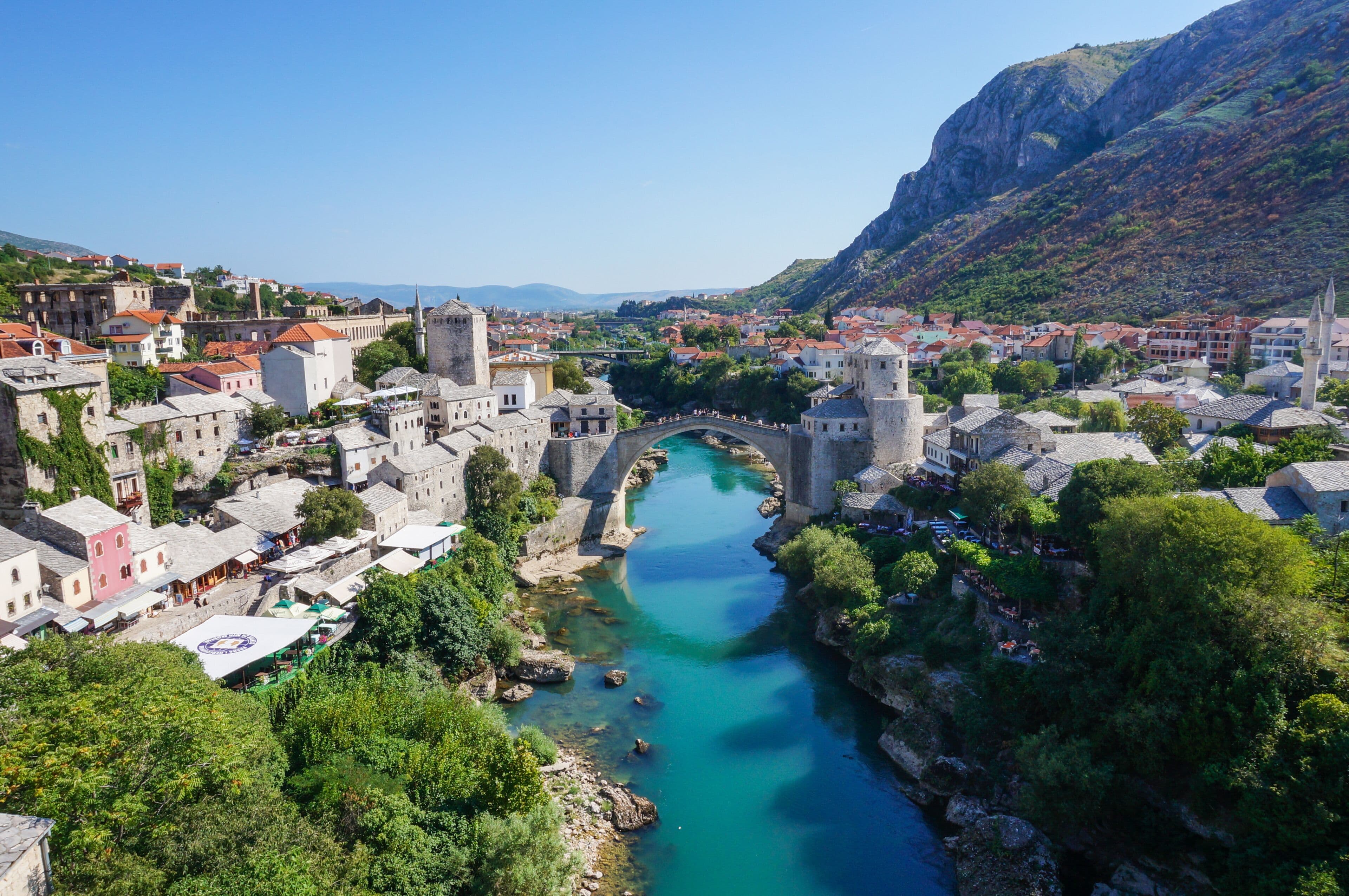 The Old Bridge of Mostar arching over the turquoise Neretva, with the stone old town on both banks in warm afternoon light